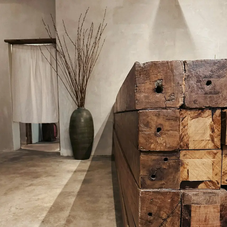 A stack of old, hewn reclaimed beams next to a vase of dry branches