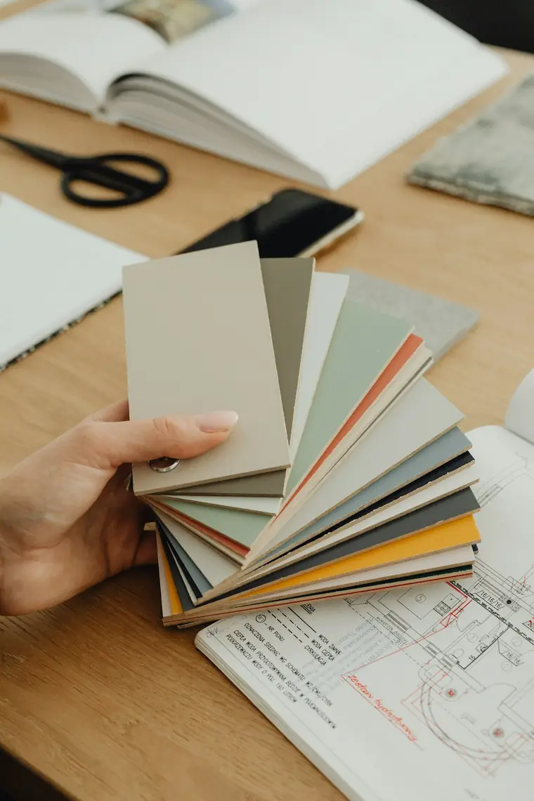A hand holding a fan of color swatches over spread-out technical drawings