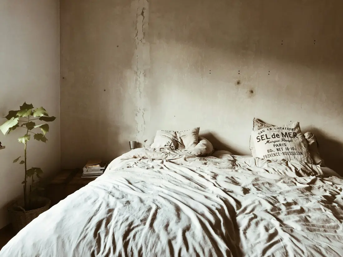 A bedroom with linen bedding against a wall of exposed, unpainted lime plaster
